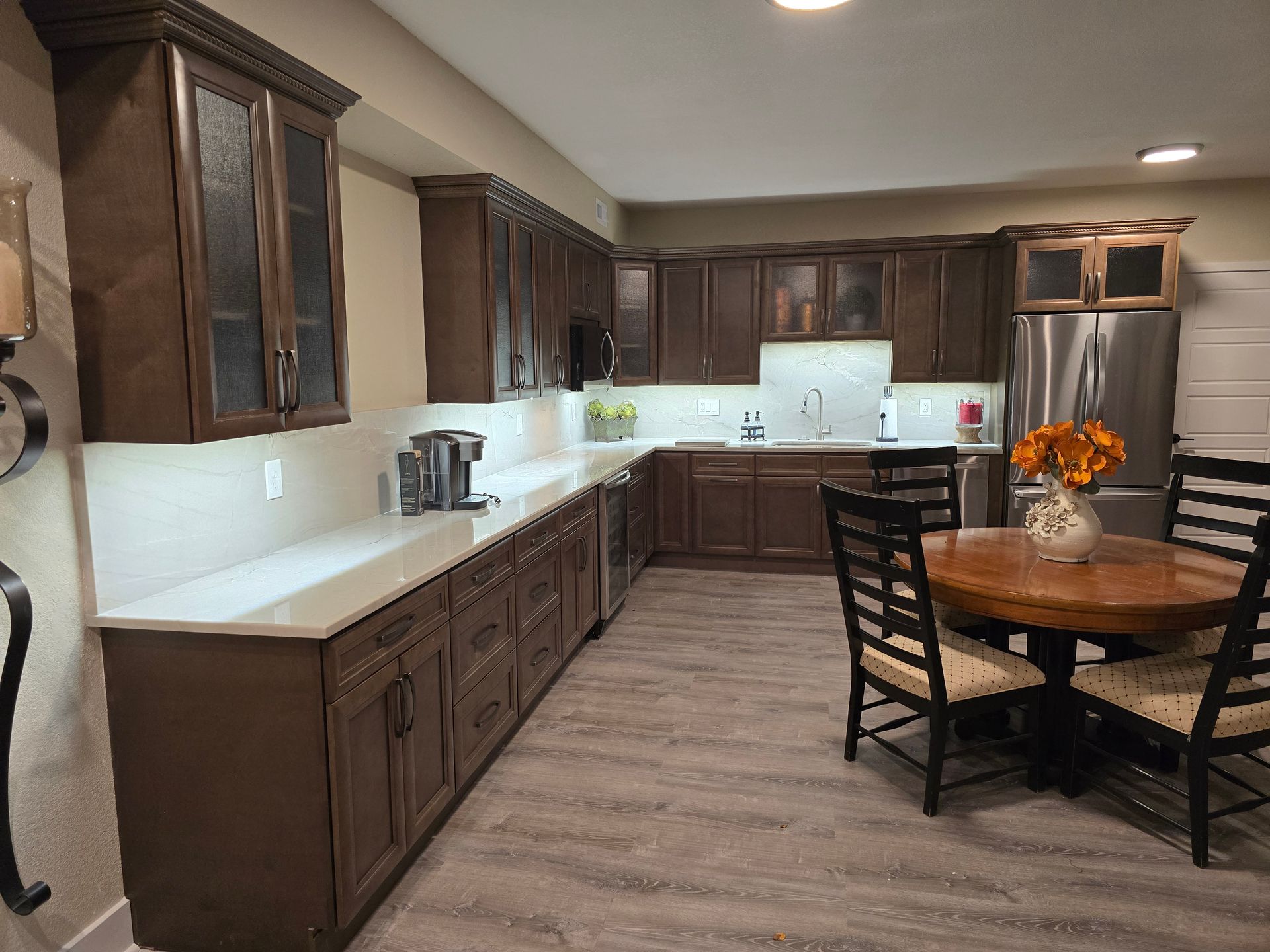 Dark brown kitchen cabinets with light countertops. Round dining table with chairs.