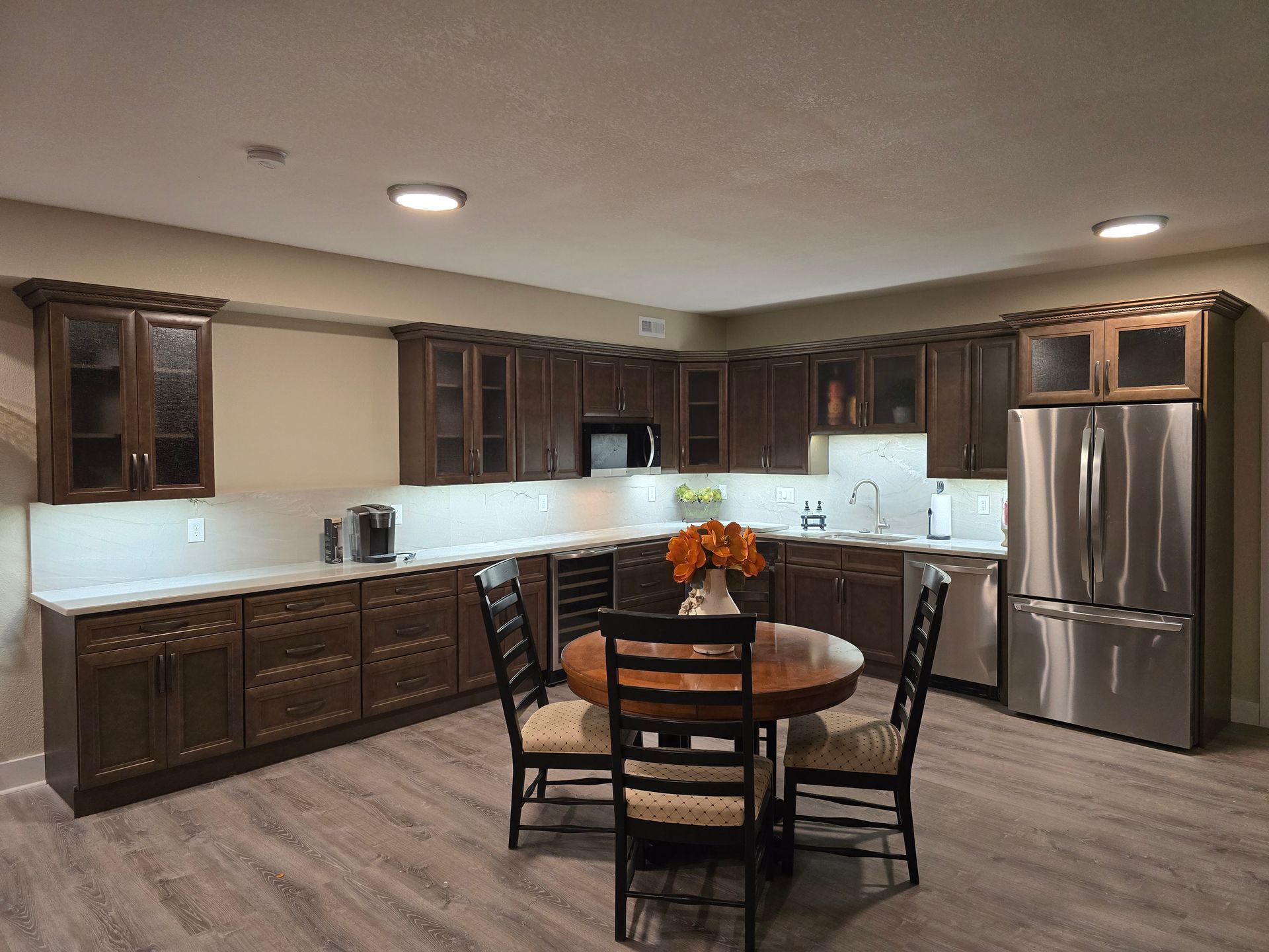 Dark brown kitchen with stainless steel appliances and a round wooden table with chairs.