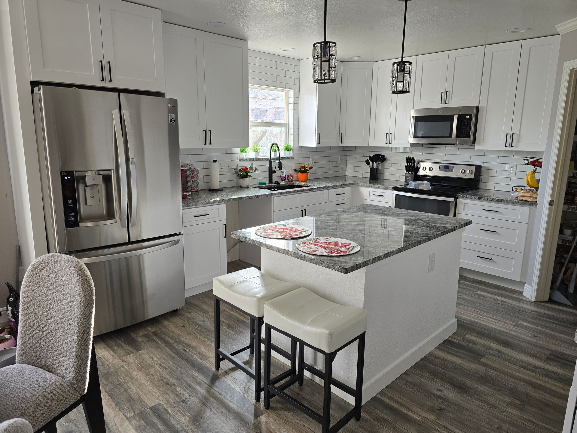 Modern white kitchen with stainless steel appliances, gray island, and stools.