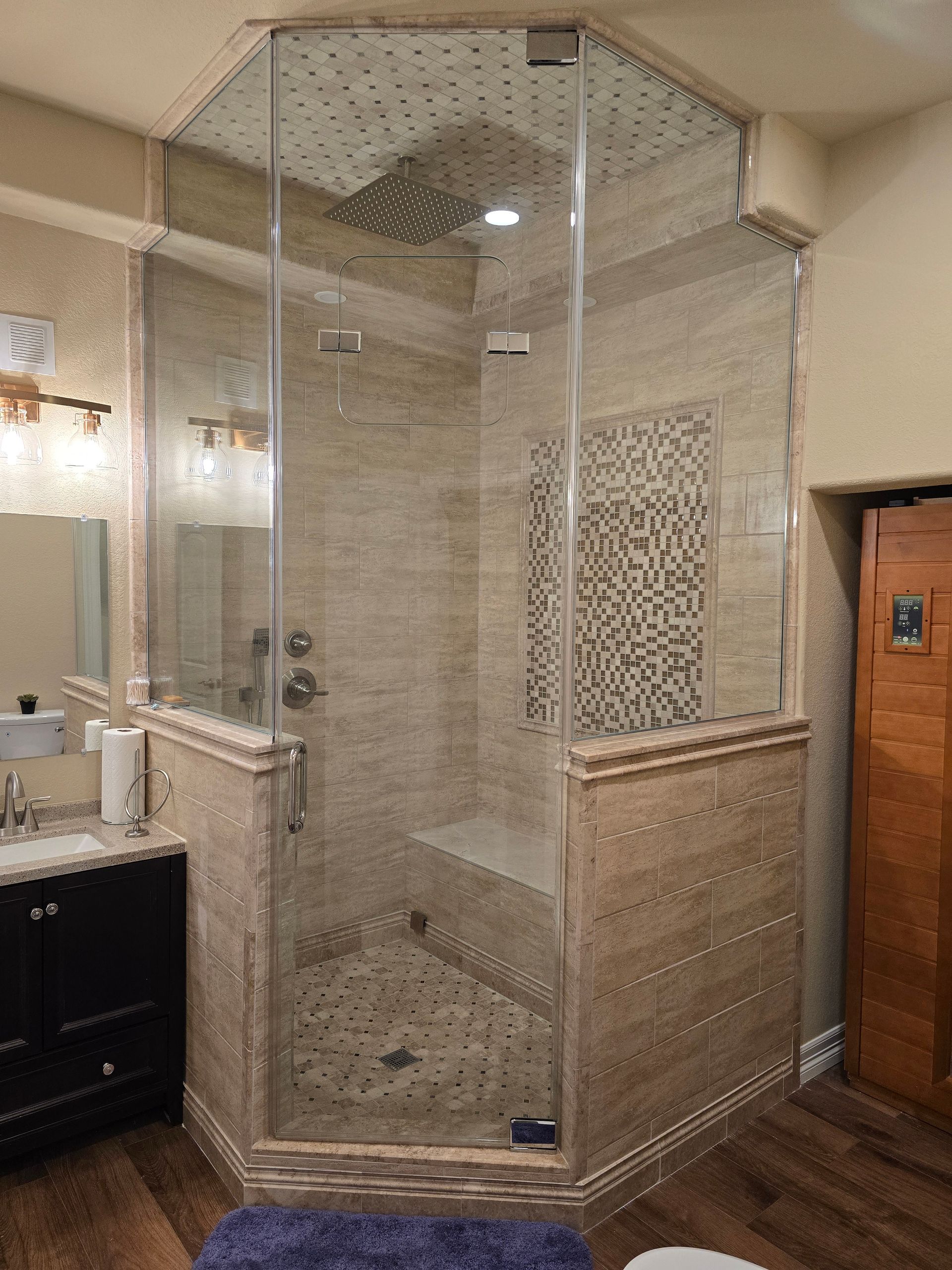 Corner shower with glass doors, beige tile walls, and a small bench.