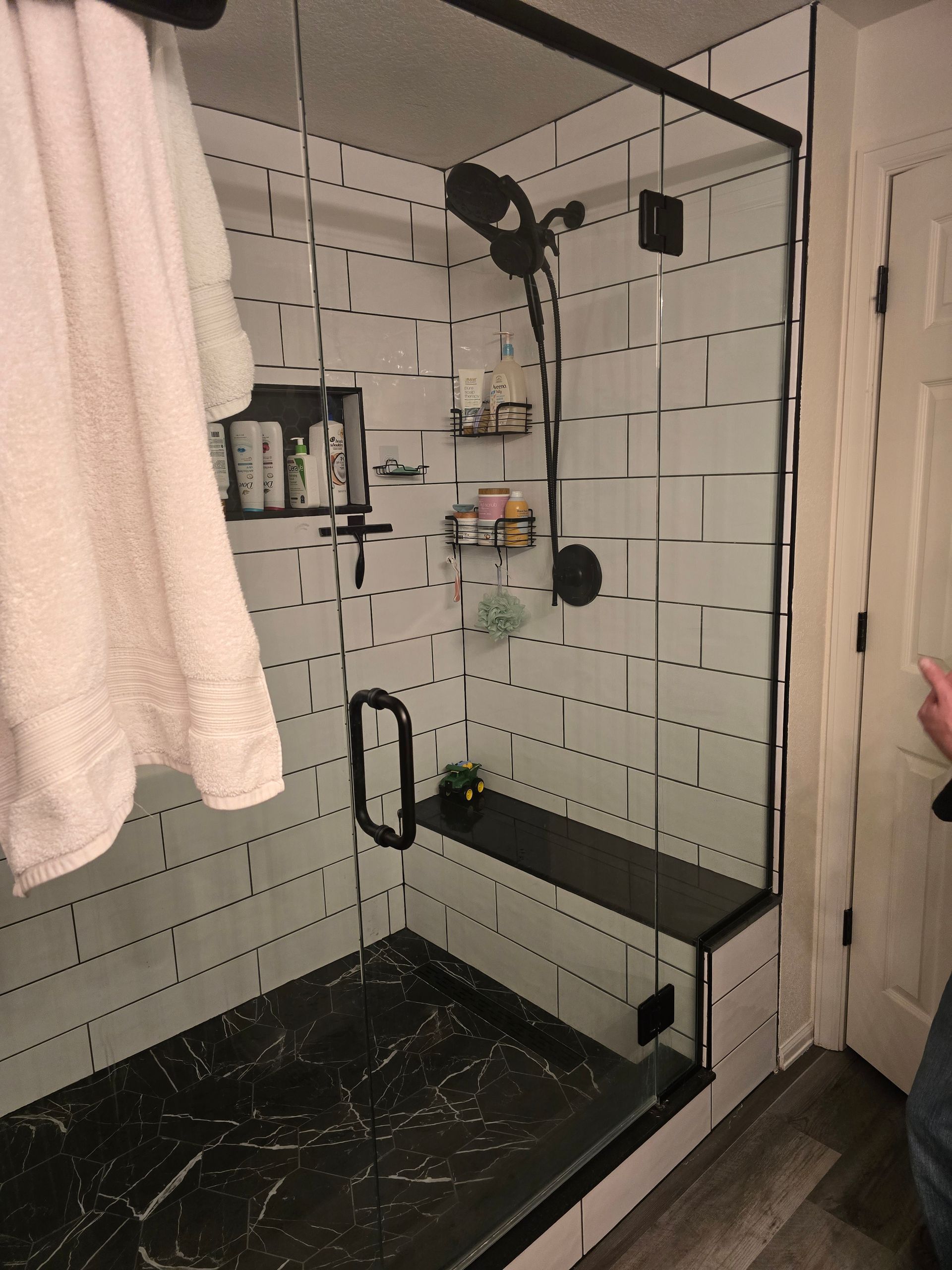 Modern black and white tiled shower with glass door, bench, and built-in shelves.