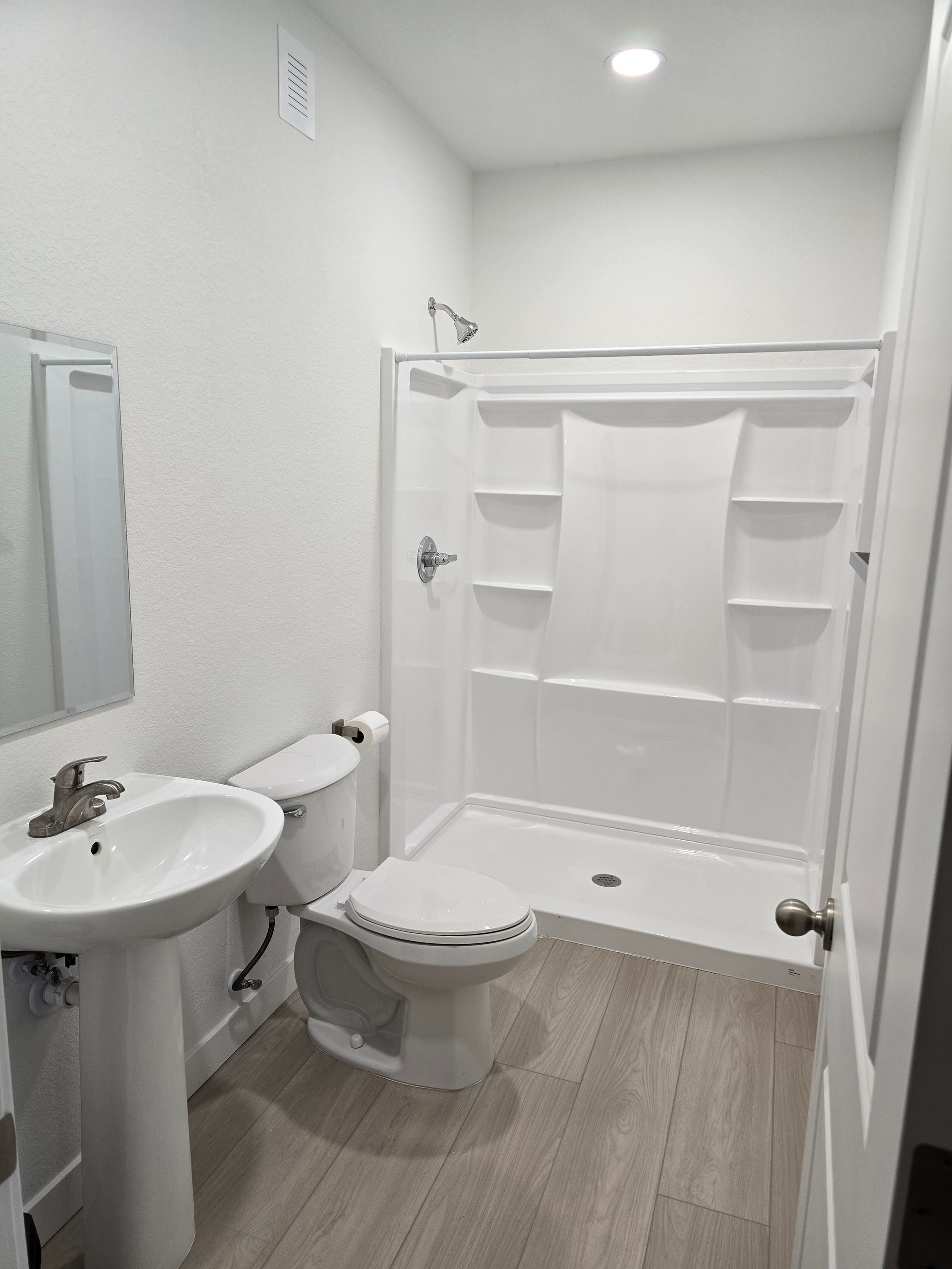 Bathroom with white walls, shower, toilet, pedestal sink, and gray floor.
