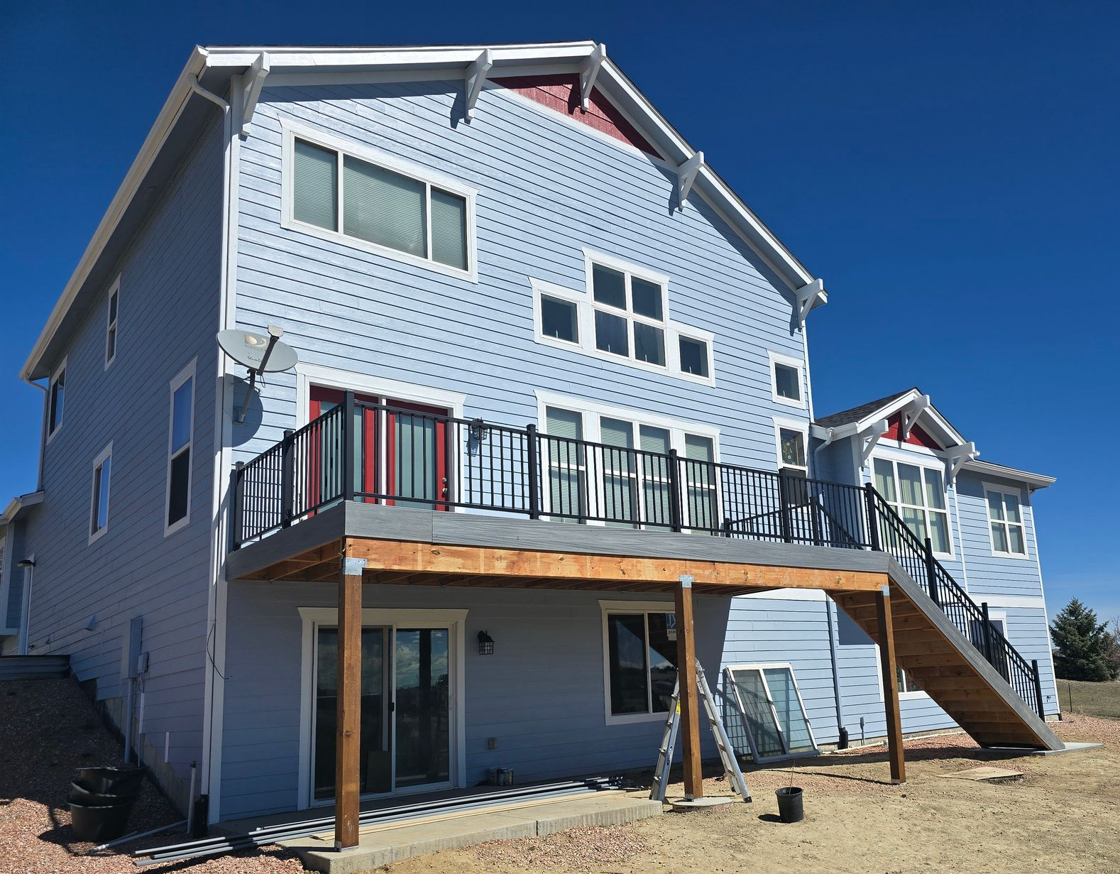 Two-story house with light blue siding and a wooden deck, set against a clear blue sky.