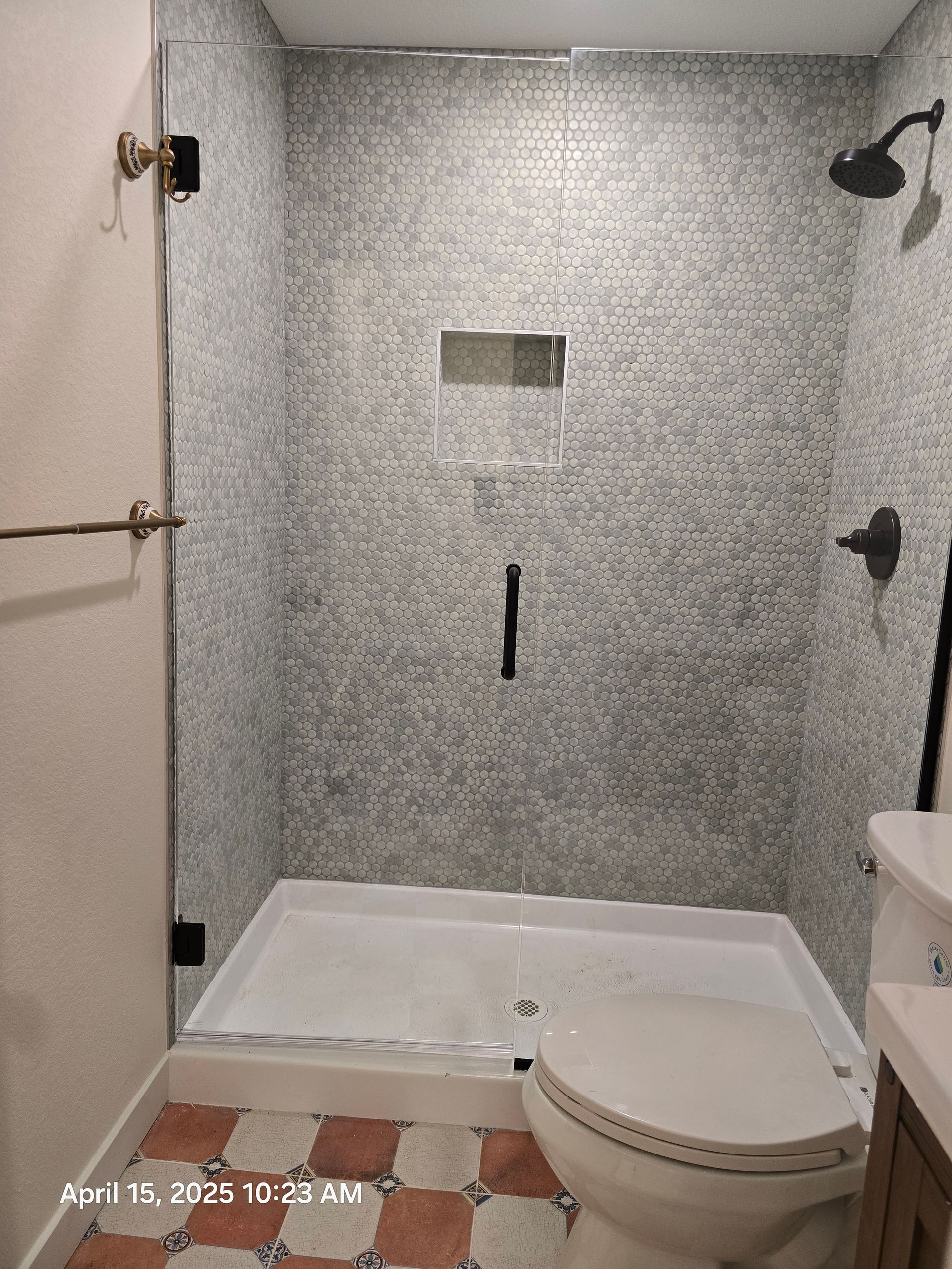 Shower with patterned gray tile walls and a clear glass door, next to a toilet and a vanity.