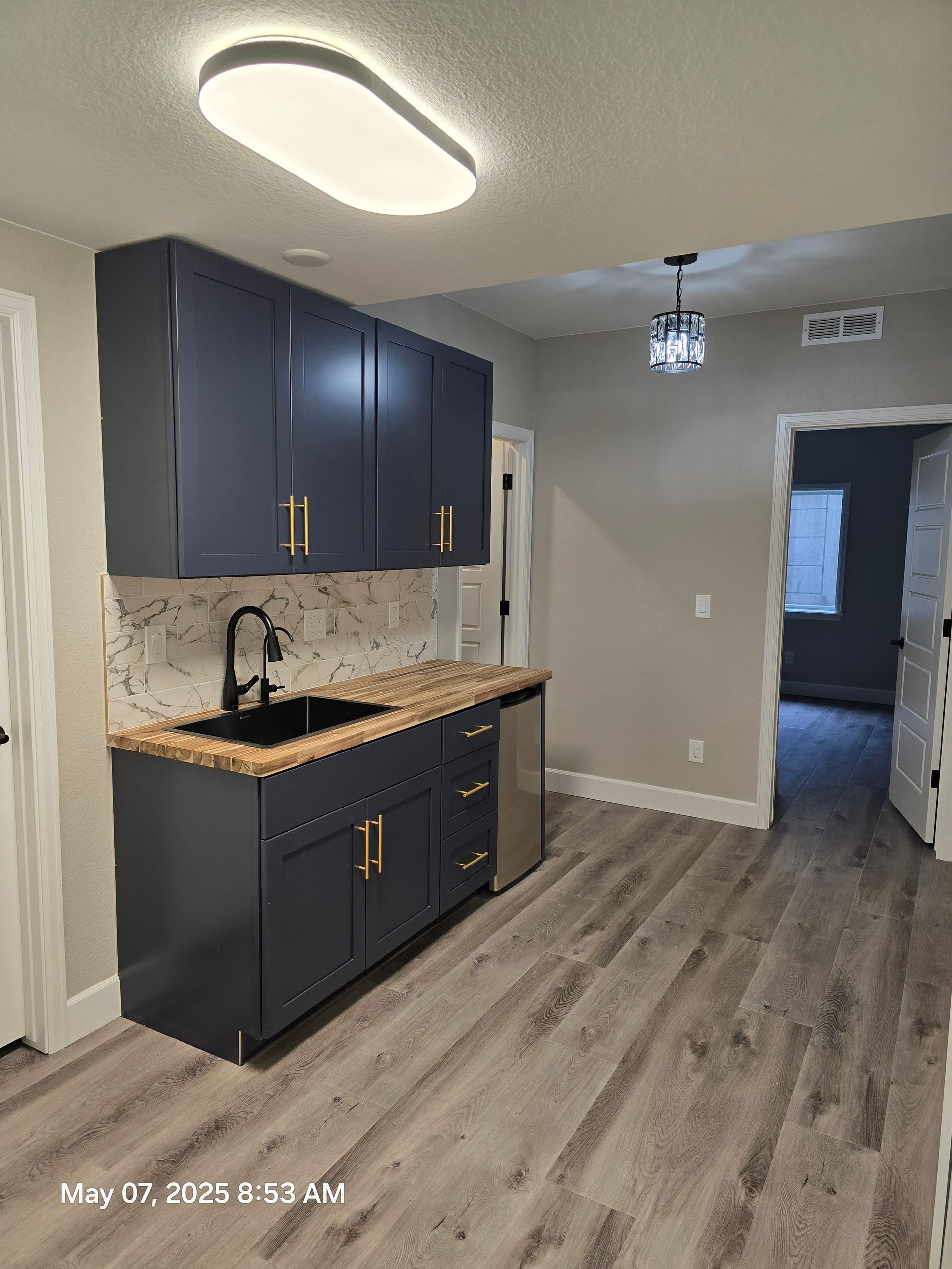 Navy blue kitchen cabinets with gold hardware and light wood countertops.