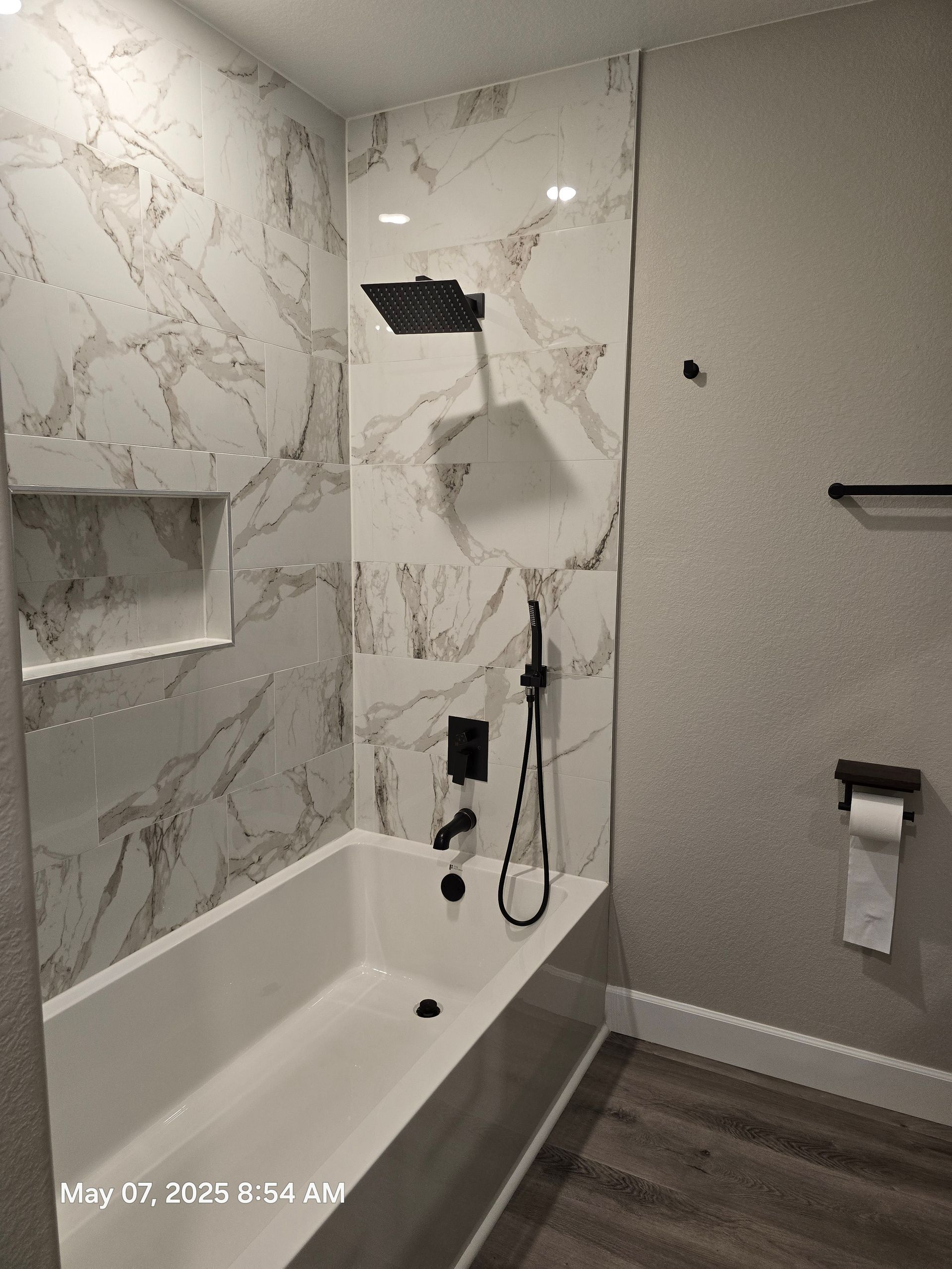 Bathroom with white marble-look tile, black fixtures, and a white bathtub.