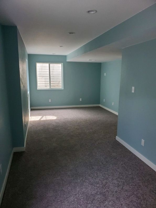 Empty room with blue walls, gray carpet, a window, and white trim.