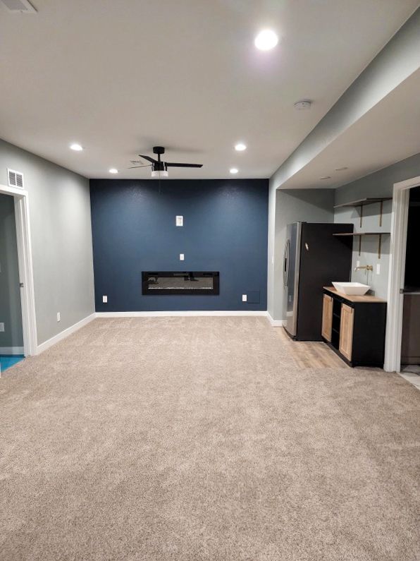 Empty basement living room with blue accent wall, fireplace, and bar area.