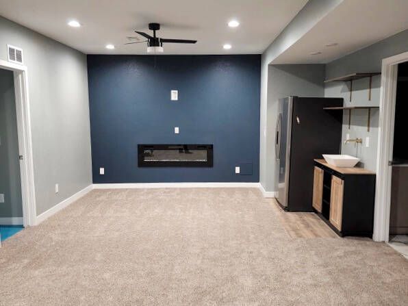 Empty modern living room with blue accent wall, fireplace, and mini-kitchenette.