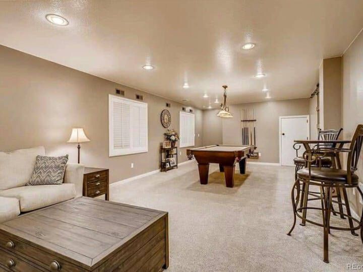 Spacious finished basement with a pool table, seating area, and bar stools. Beige walls and carpet.