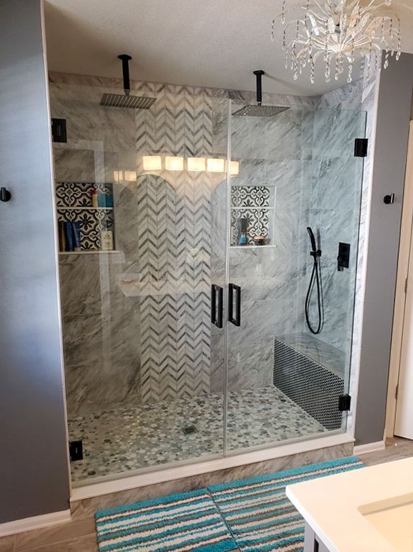 Spacious glass shower with marble walls, patterned tile accent, dual shower heads, and seating.