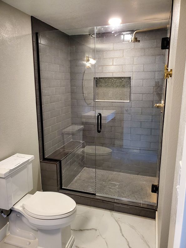 Bathroom with gray tiled shower, glass door, toilet, marble floor.