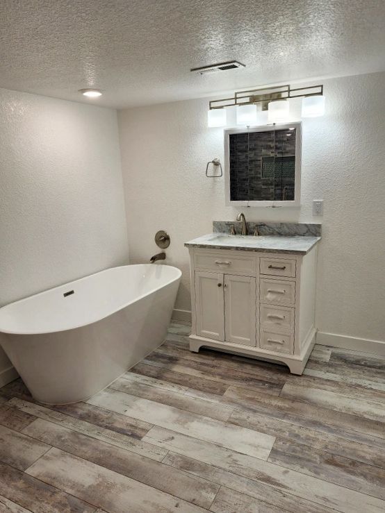 Modern white bathroom with freestanding tub, white vanity, and wood-look floor.