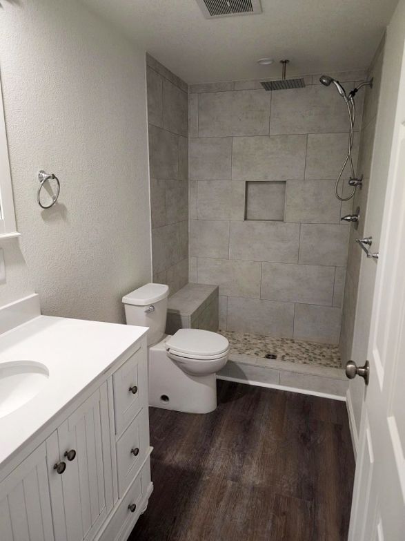 Bathroom with white vanity, toilet, tiled shower, and dark wood flooring.