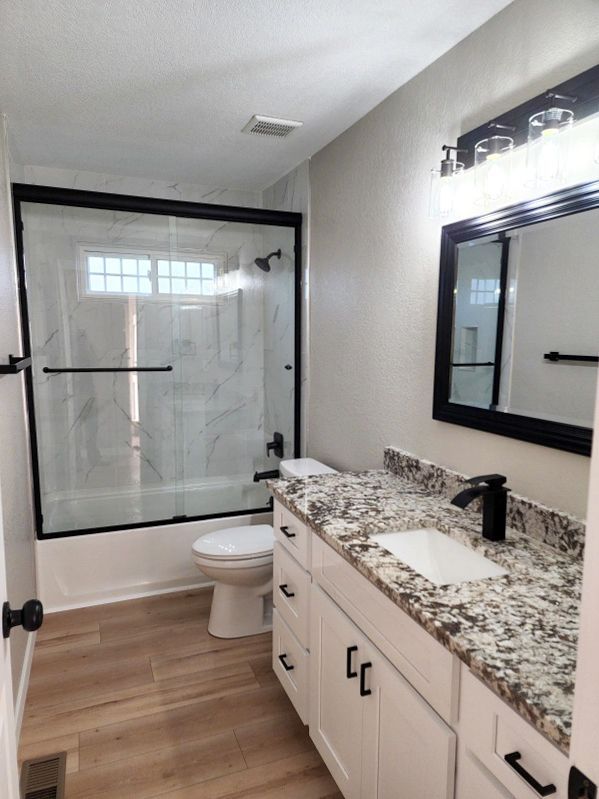 Bathroom with white vanity, patterned countertop, black fixtures, shower, and wood-look flooring.