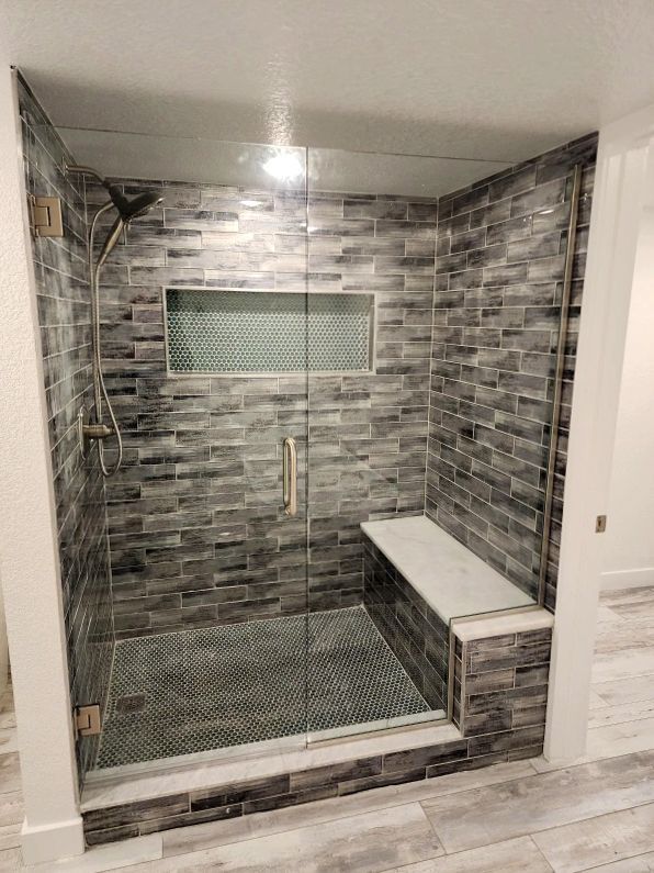 Gray tiled shower with glass doors, built-in bench, and shelf.