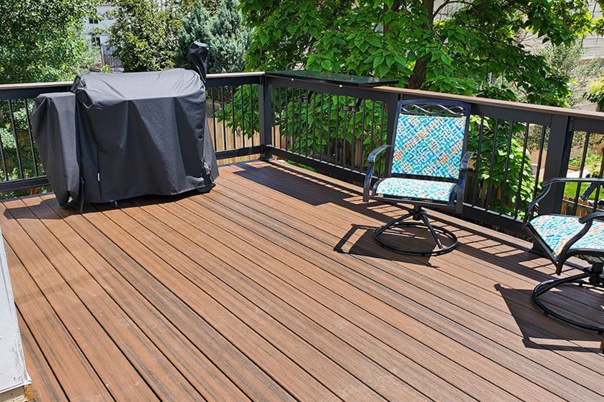 A wooden deck with a grill and chairs on it.