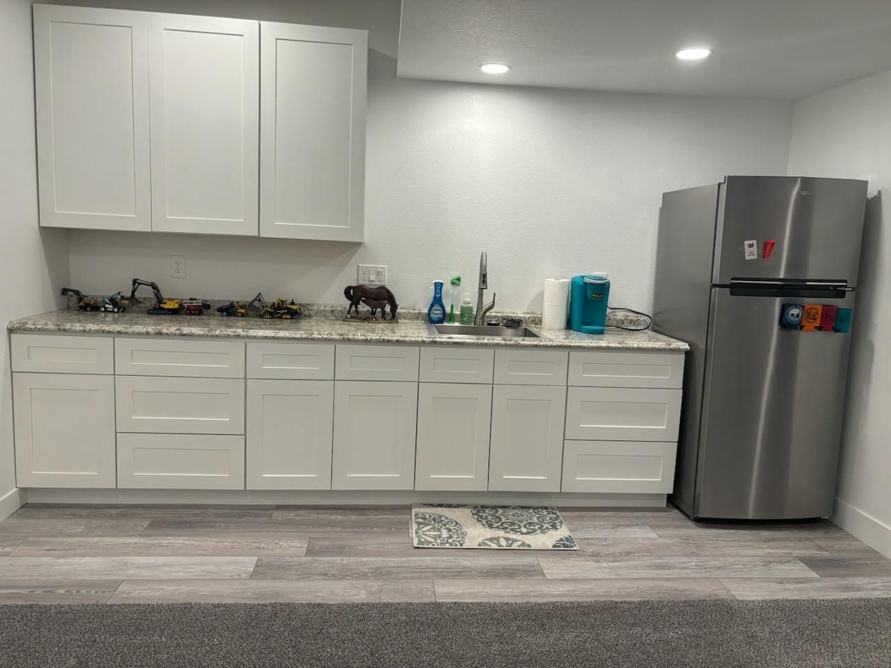 Kitchen with white cabinets, granite countertop, sink, and stainless steel refrigerator.
