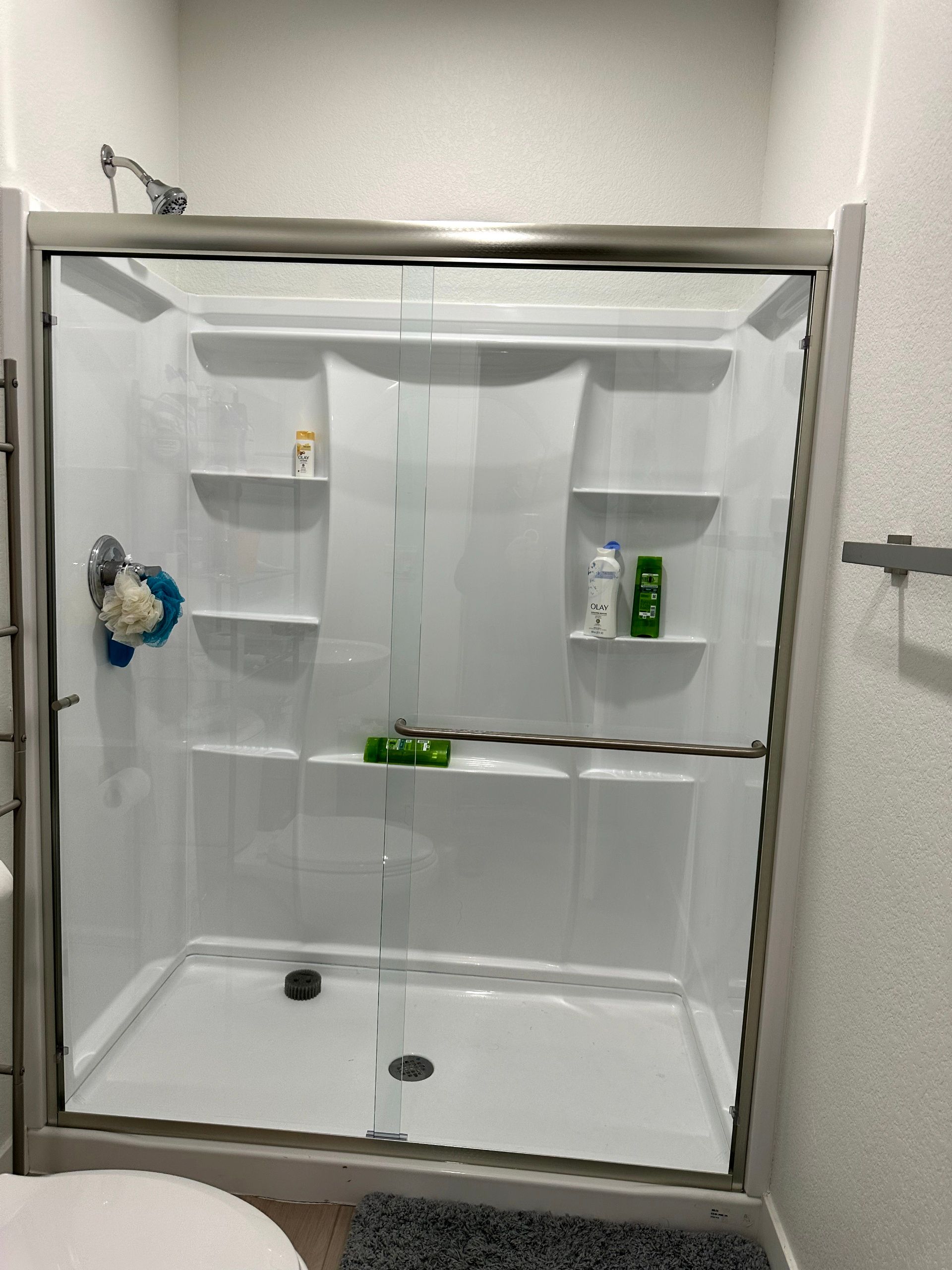 White shower stall with sliding glass doors, shelves holding toiletries.