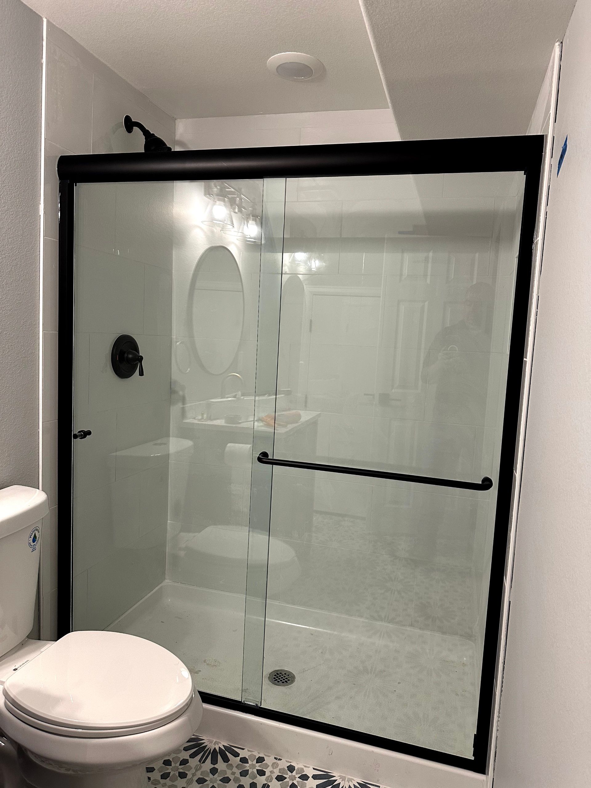 Bathroom with black-framed shower, toilet, and sink. White walls, grey flooring.