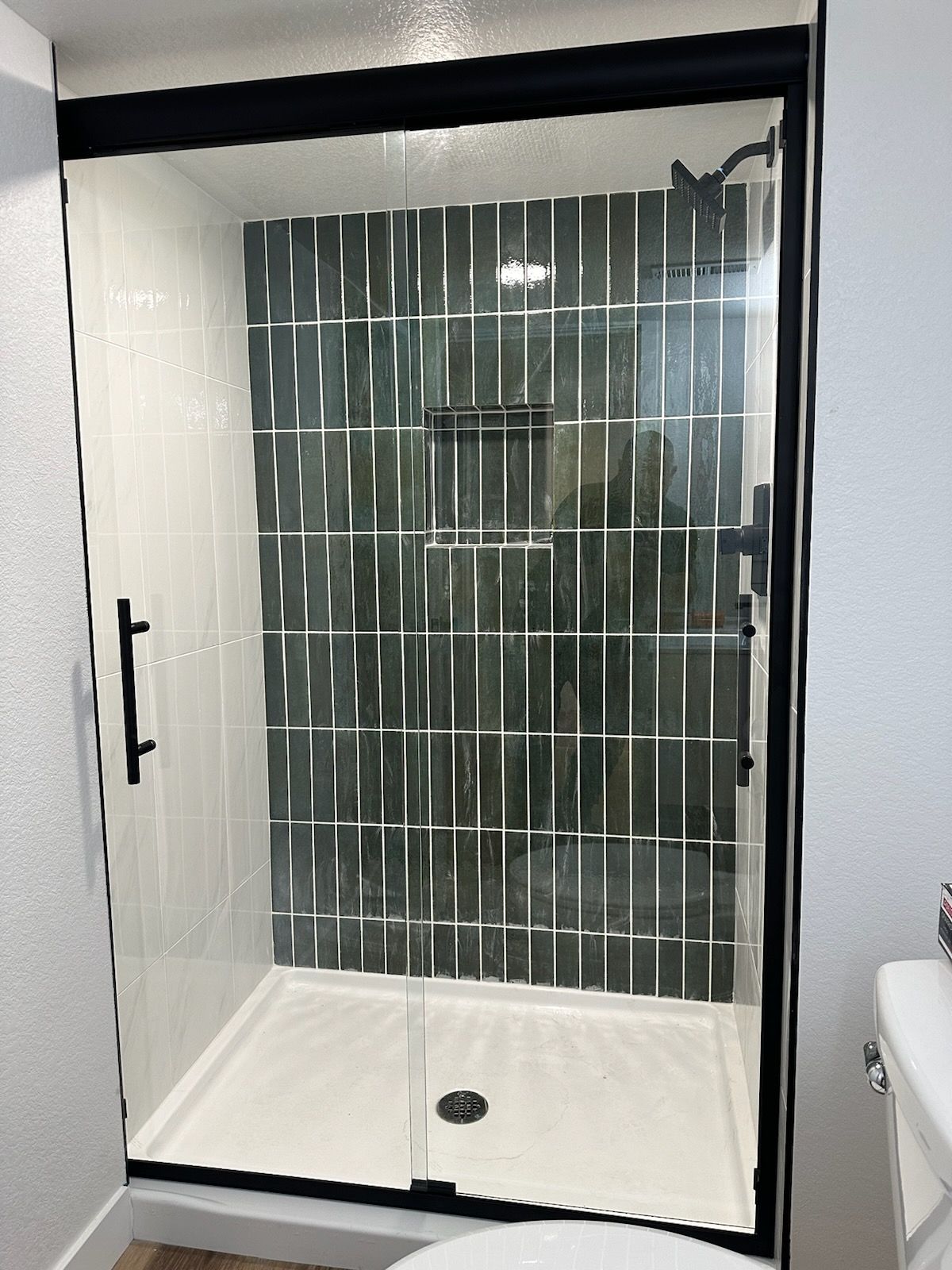 Modern shower with black trim, glass door, and dark green tile accent wall.