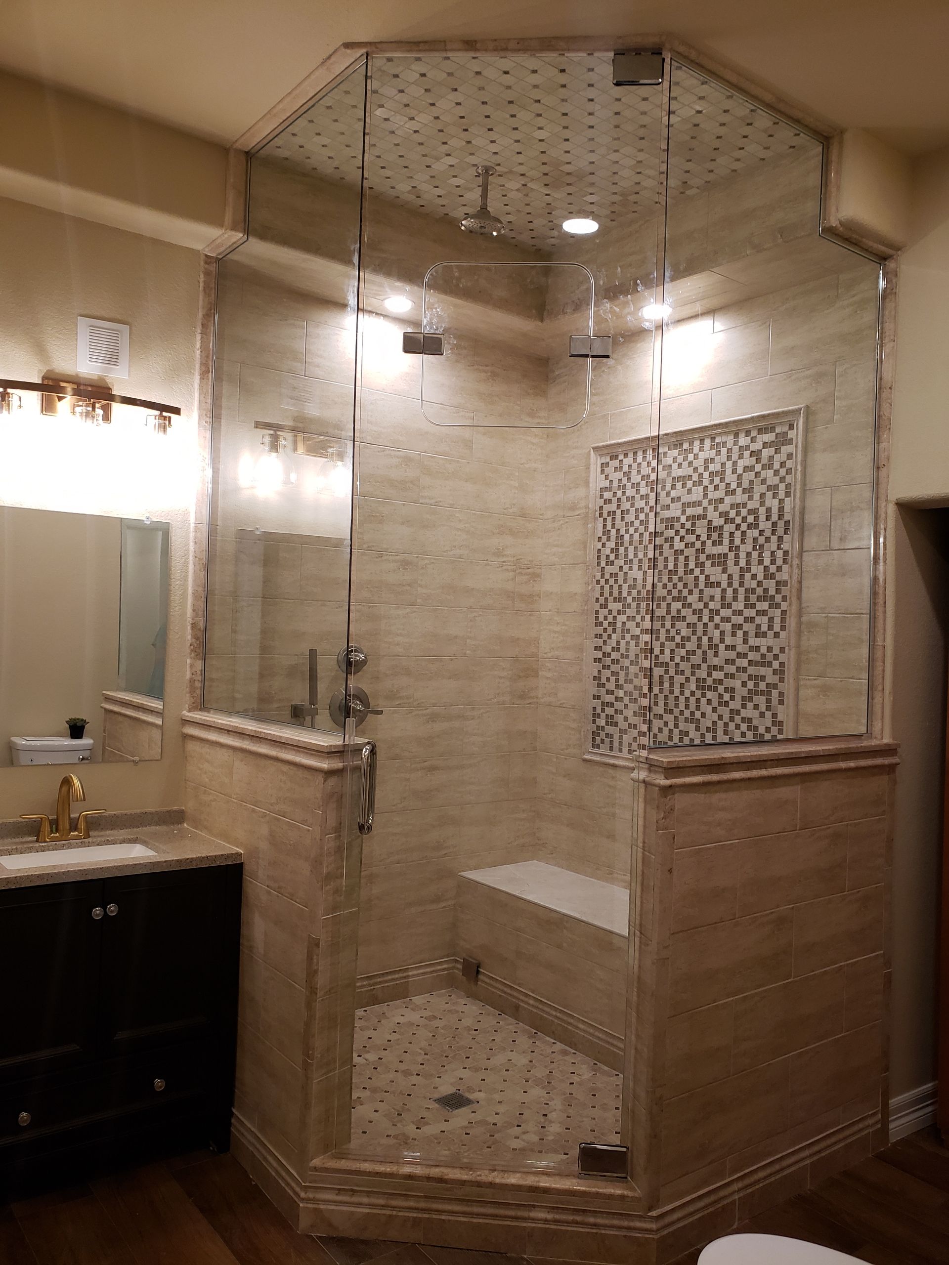 Modern tiled shower with glass walls and ceiling, bench, and fixtures.