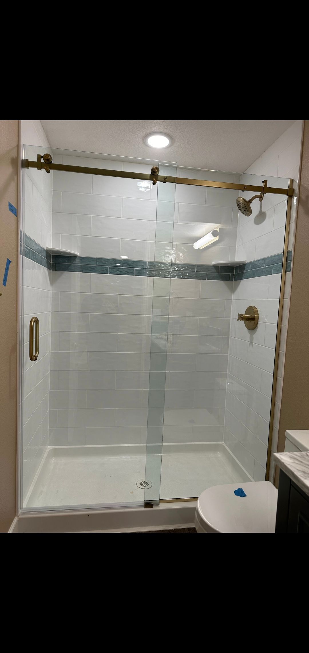 Shower with glass doors, brass fixtures, and white and teal tile accents.