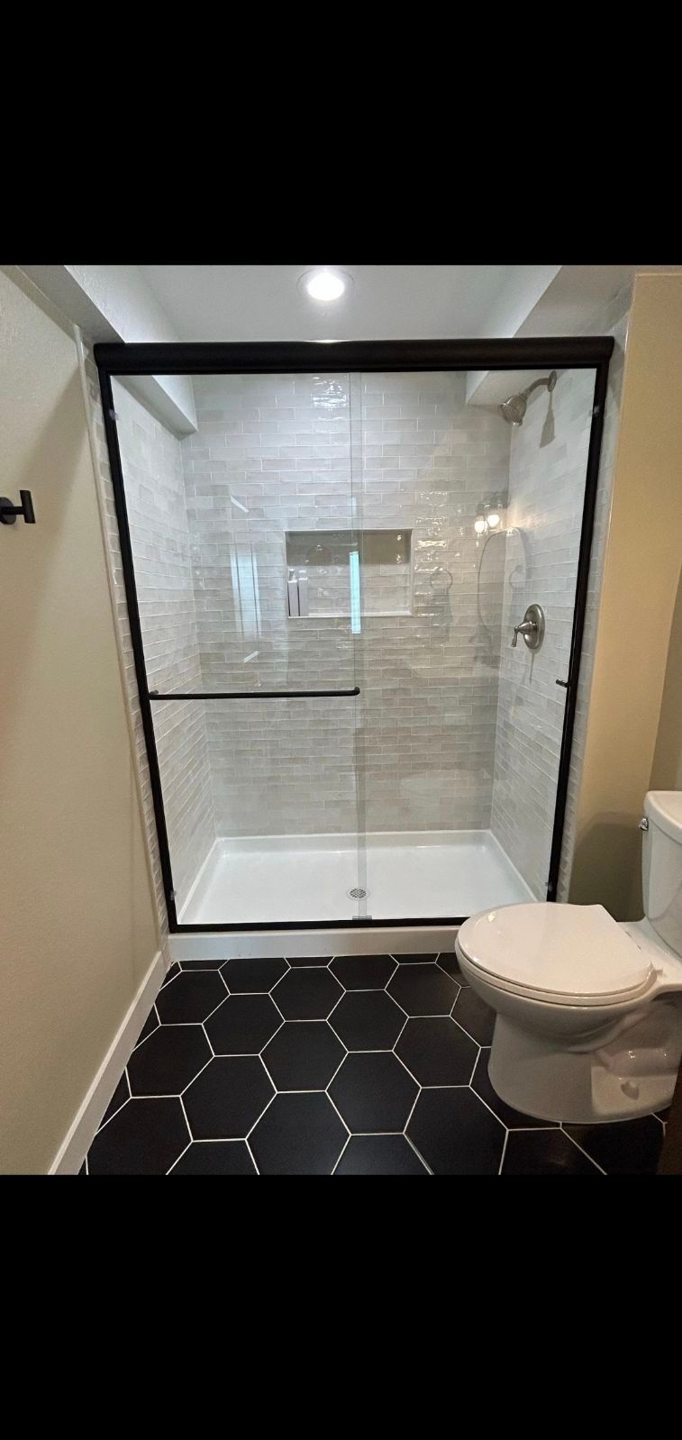 Bathroom with black hexagon tile floor, glass shower, and white toilet.