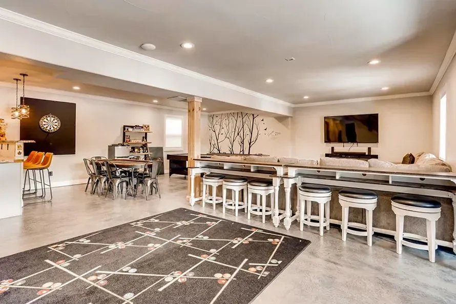 Spacious finished basement with dining, bar, and lounge areas; a rug covers the concrete floor.