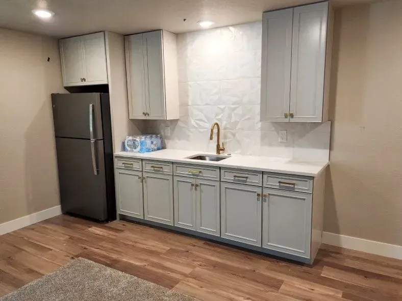 Light blue kitchen cabinets with a stainless steel fridge on wood flooring.