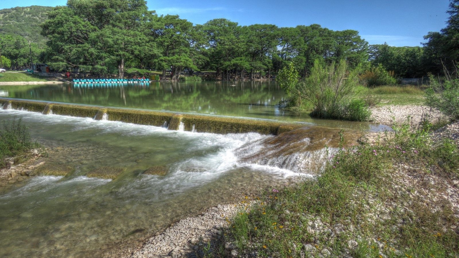 A river with a waterfall in the middle of it and trees in the background.
