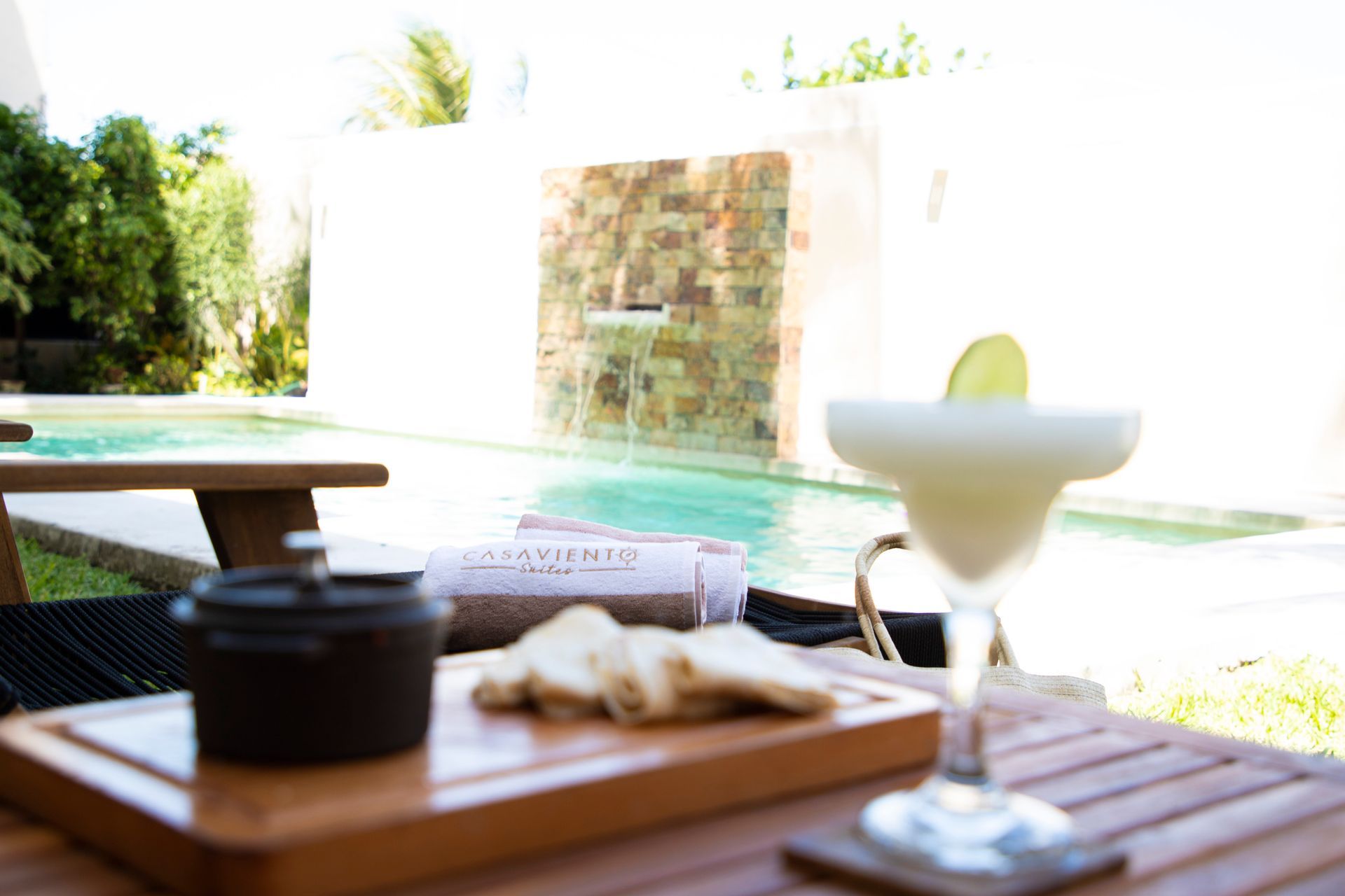 Una margarita está sentada en una mesa de madera frente a una piscina.