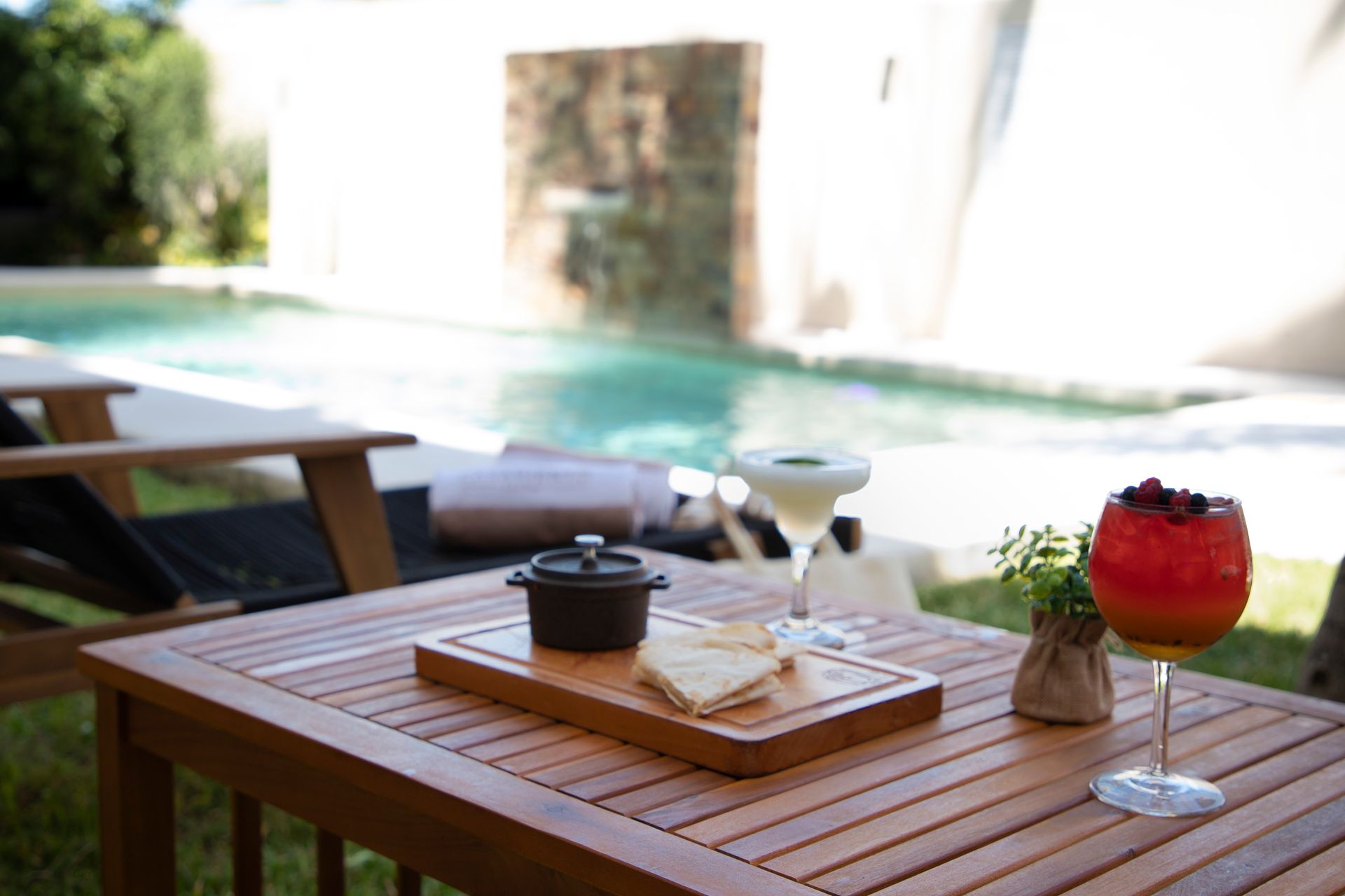 Una mesa de madera con una bandeja de comida y una bebida frente a una piscina.
