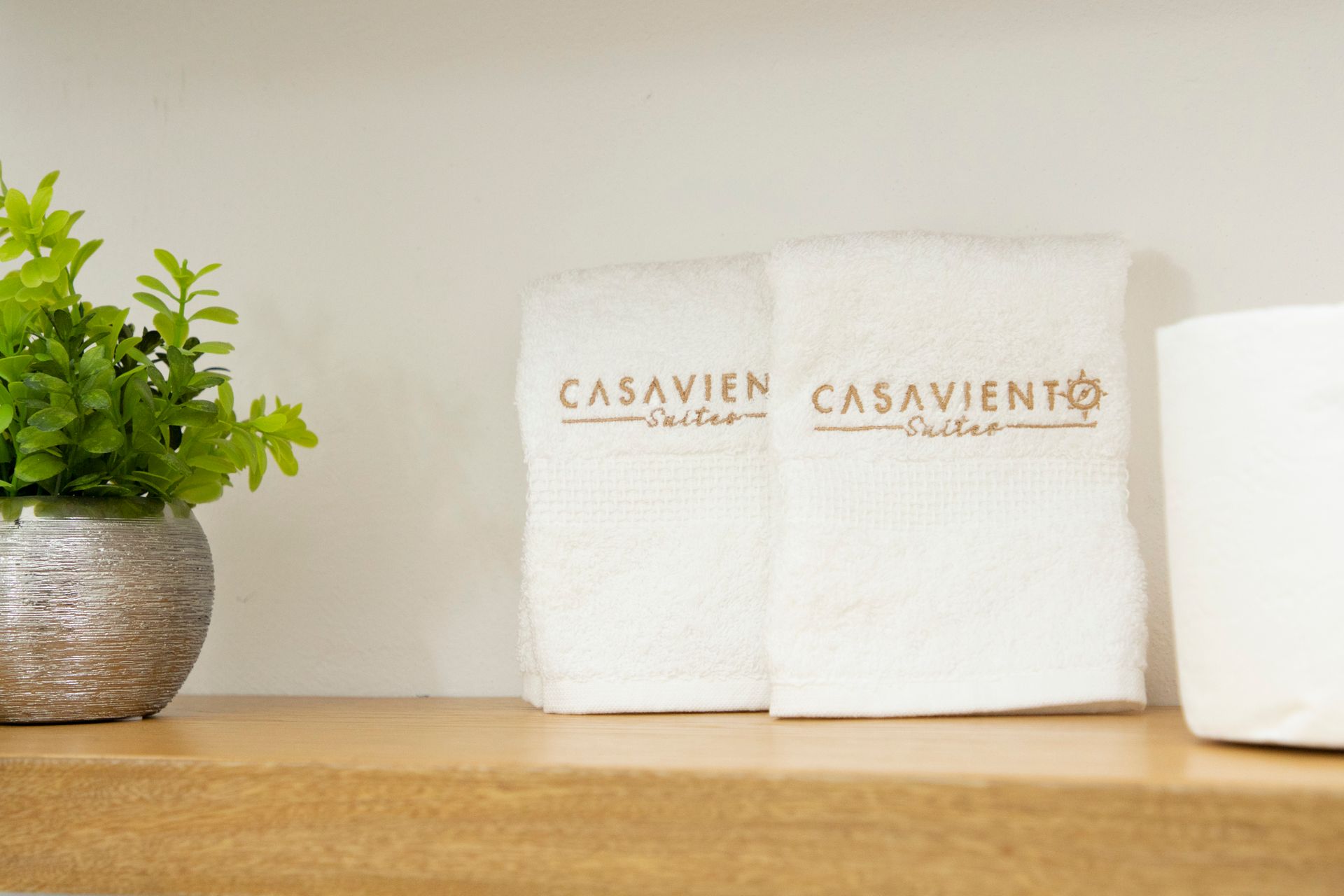 Dos toallas blancas están sobre un estante de madera al lado de una planta en maceta.