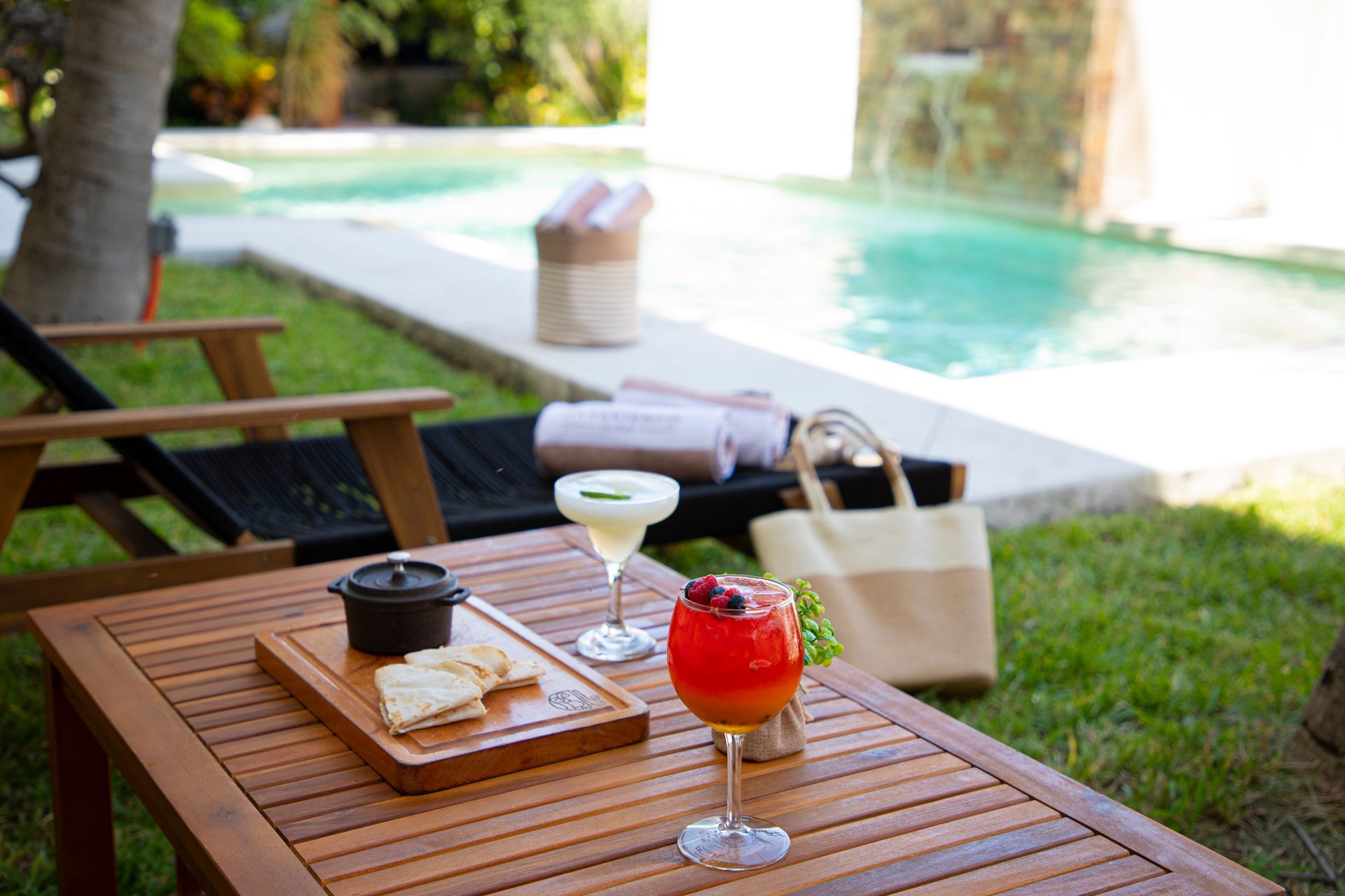 Una mesa de madera con dos bebidas frente a una piscina.