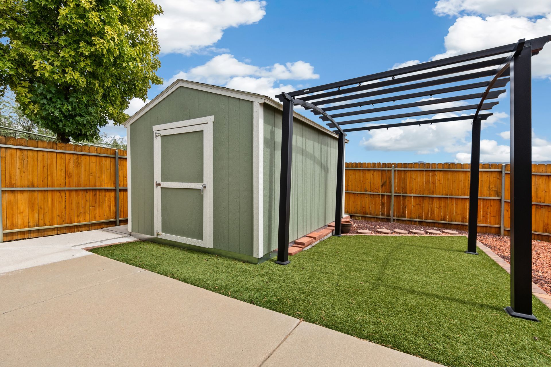 Backyard shed with green lawn and pergola under clear blue sky in a residential area.