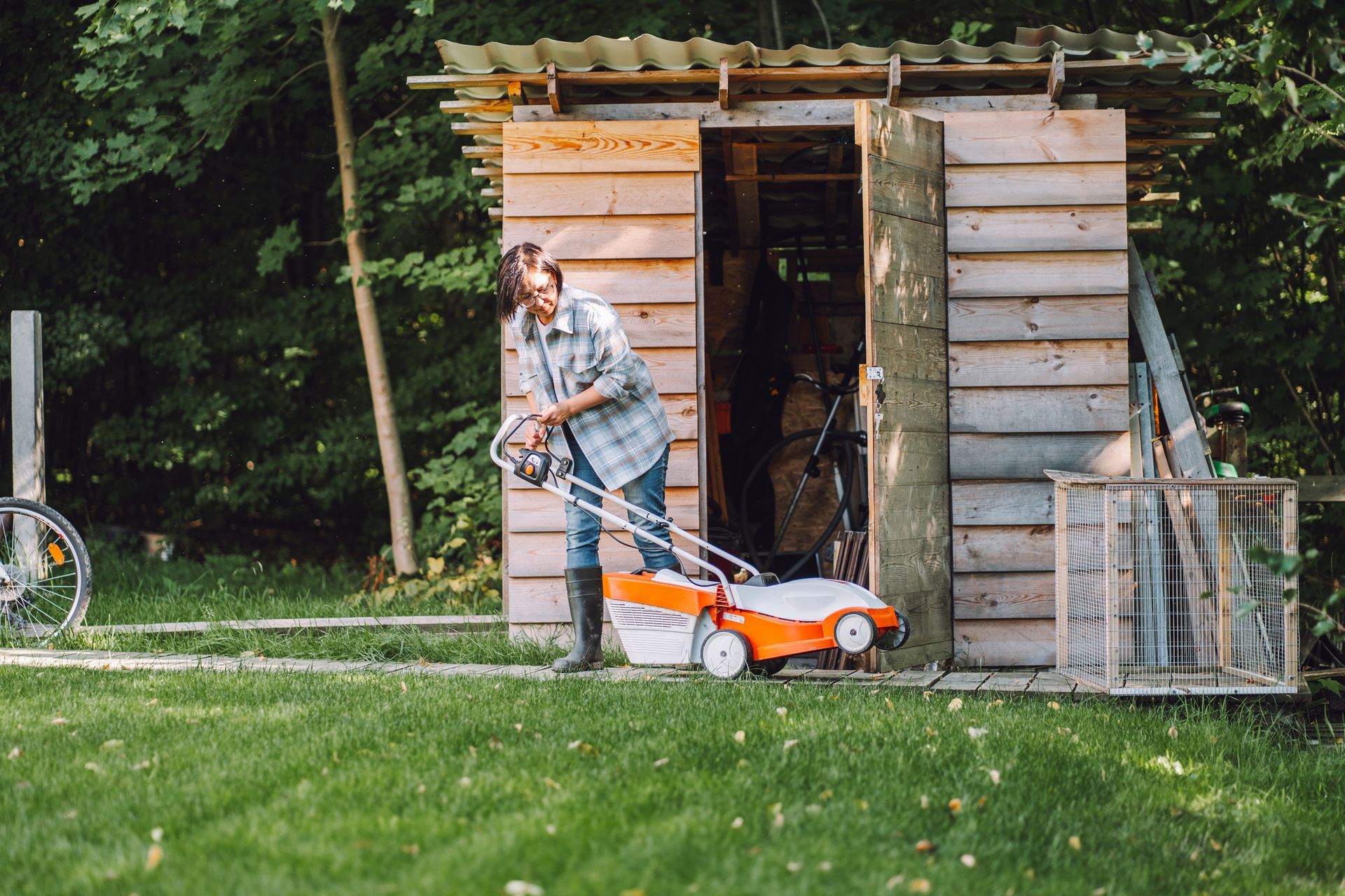 Woman taking out lawnmower from her shed in the backyard.