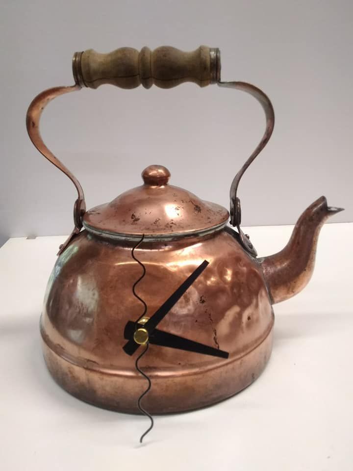 A copper tea kettle repurposed as a wall clock with black hands and a vertical wavy line on its surface.