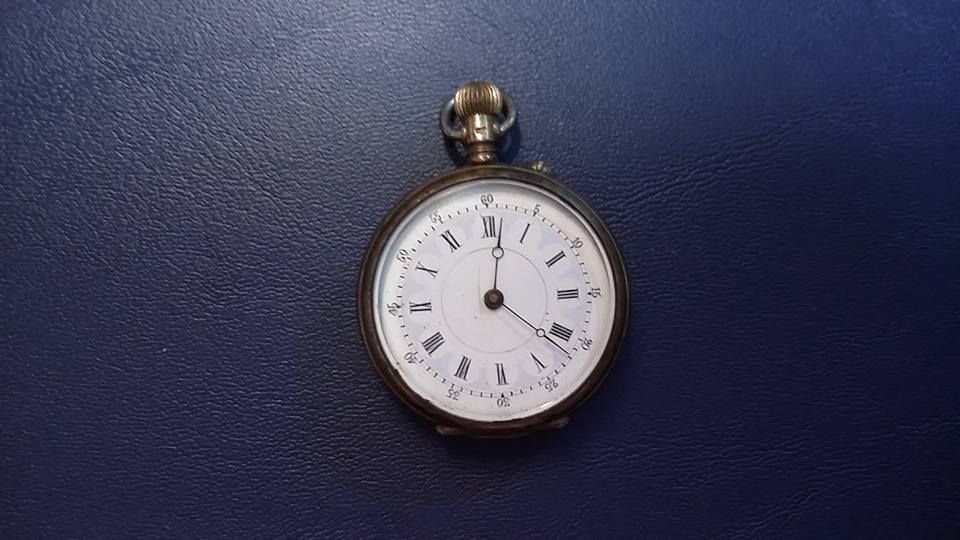 An antique pocket watch with a white face and black Roman numerals, set against a dark blue background.