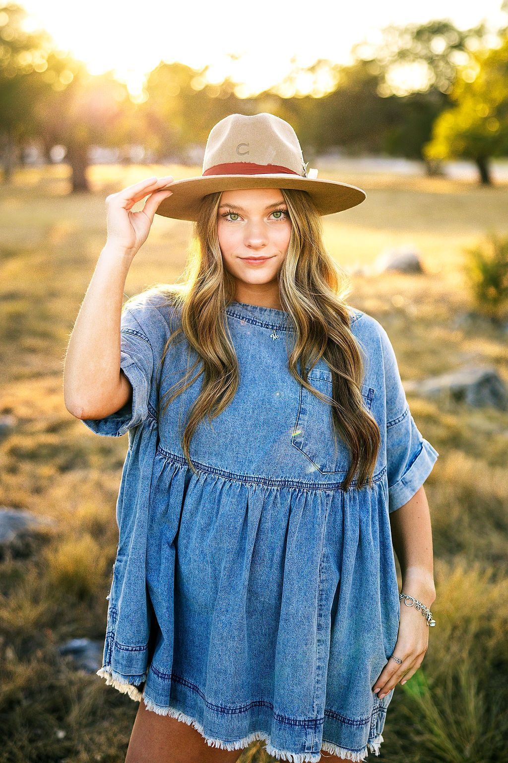 A woman in a denim dress and hat is standing in a field.