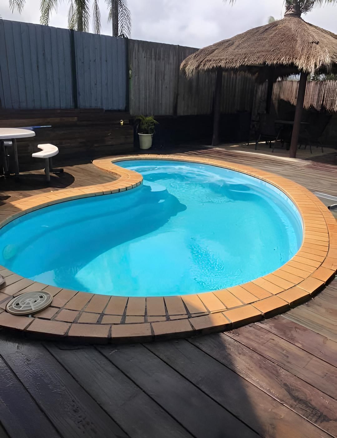 A Large Swimming Pool With A Thatched Gazebo In The Background — Aqua Duck Pool Care In Landsborough, QLD