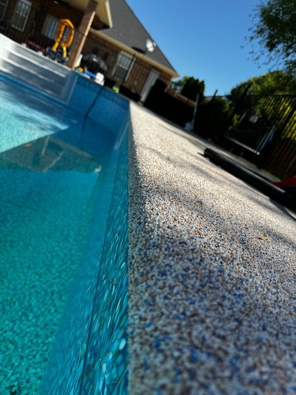 Poolside with turquoise water and speckled concrete border under a blue sky.