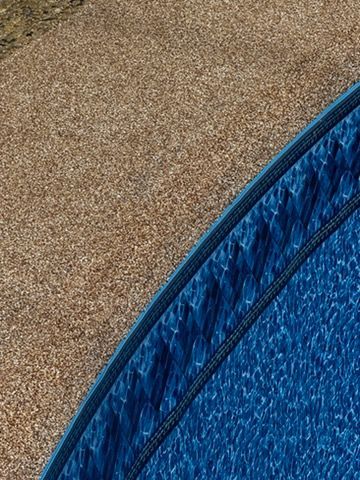 Corner of a blue swimming pool with textured water next to a beige stone surface.
