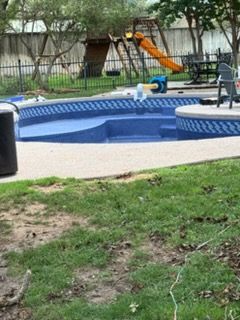 A partially constructed swimming pool with a slide, and a playground in the background.