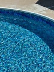Blue water in a swimming pool with a blue-tiled interior, surrounded by a concrete border.