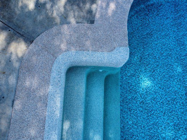 Pool steps leading into blue water, shot from above. Concrete steps with dappled light.