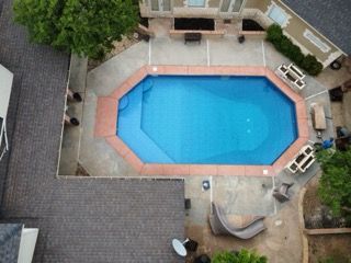 Aerial view of a blue, octagon-shaped pool surrounded by a brick border and patio.