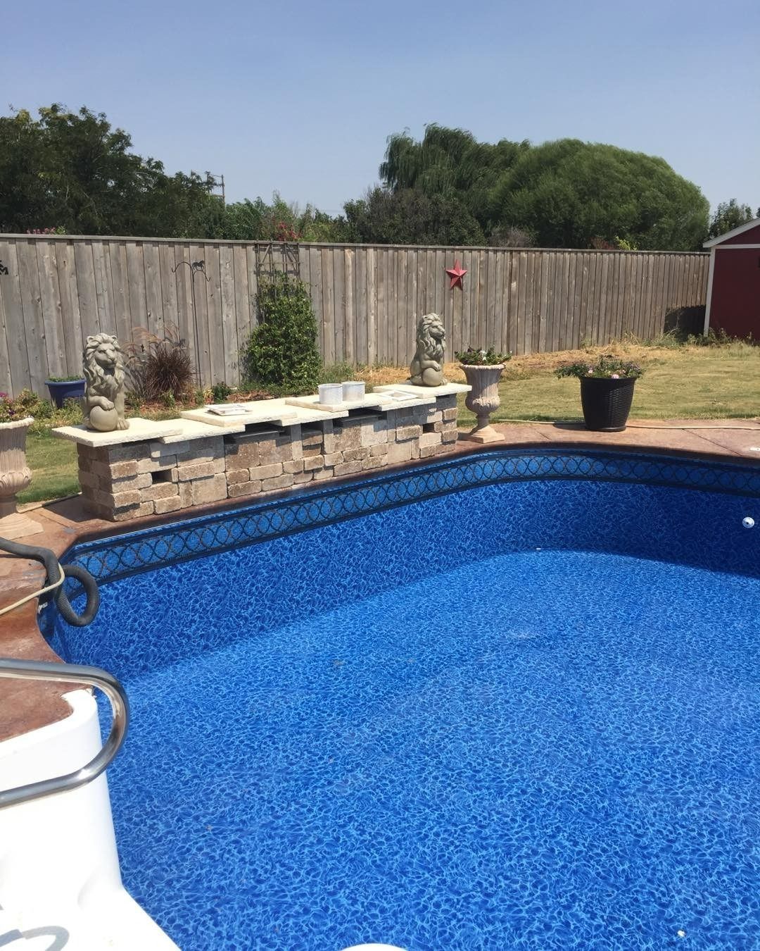 Blue-tiled swimming pool with a stone wall and fence in the background, on a sunny day.