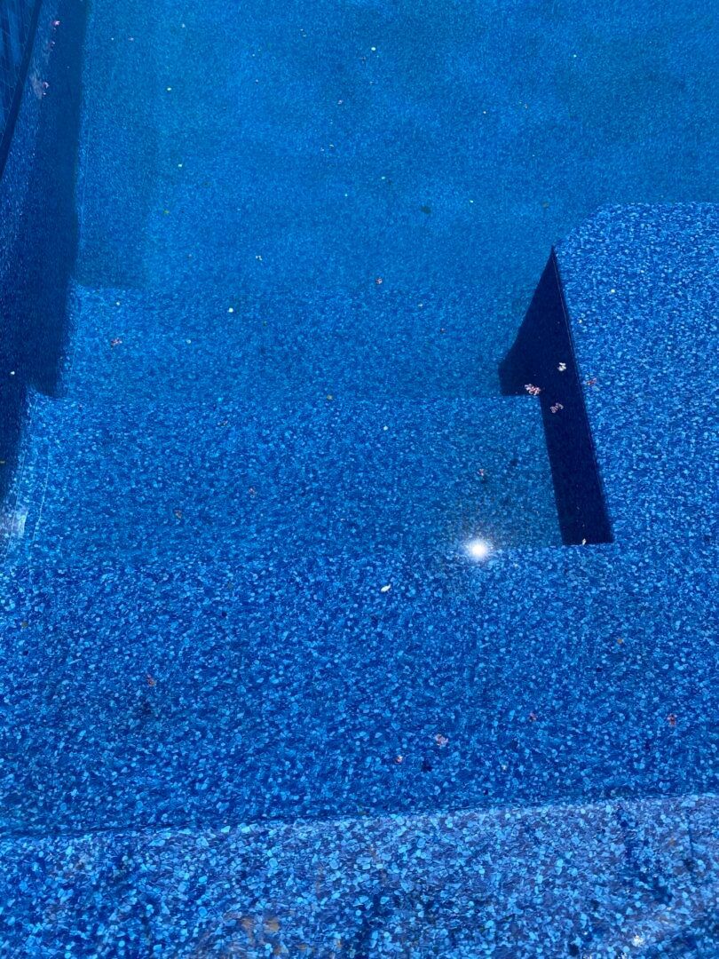 Blue-tiled pool with steps partially submerged in water, sparkling in the light.