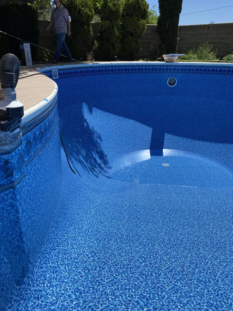 Blue tiled swimming pool with a man walking in the background. Sunny day.